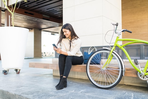 Full length of female office worker using mobile phone by green bicycle