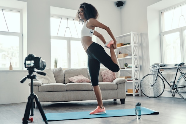 Full length of fit and beautiful young African woman working out and smiling while making social media video