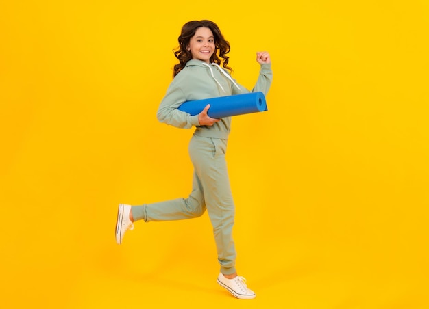 Full length of a fitness teen girl in sportswear hold yoga mat posing over yellow background Run