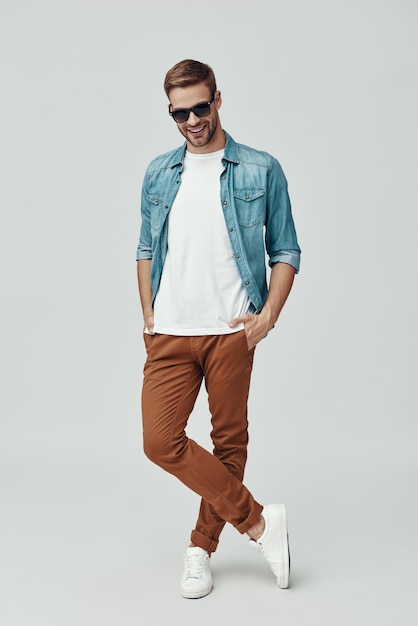 Full length of handsome young man looking at camera and smiling while standing against grey background