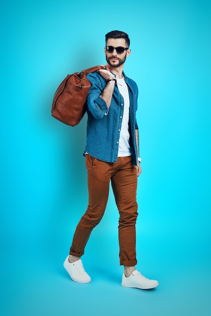 Full length of handsome young man smiling and looking away while walking against blue wall