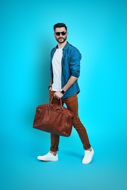 Full length of handsome young man smiling and looking at camera while walking against brown wall