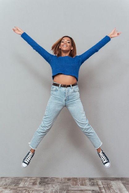 Full length happy african woman in sweater and jeans jumping