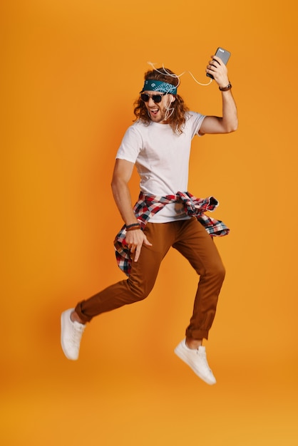 Full length of happy young man listening music and smiling while hovering against yellow wall