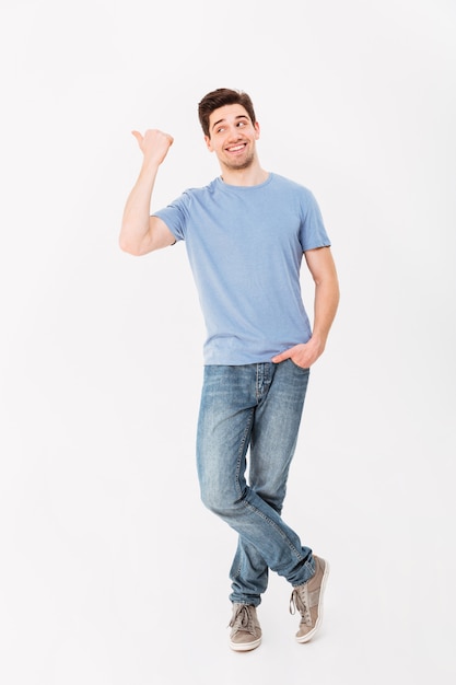 Full-length image of man in good mood presenting text or product with pointing finger aside on copyspace, isolated over white wall