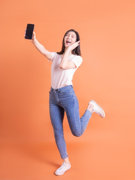 Full length image of young Asian girl using smartphone on orange background