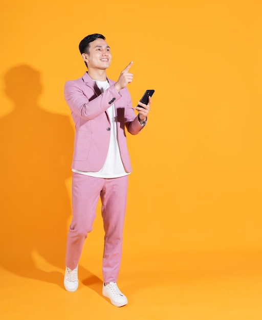 Full length image of young Asian man standing on orange background