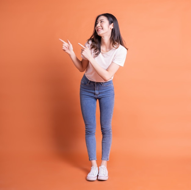 Full length image of young Asian woman posing on orange background