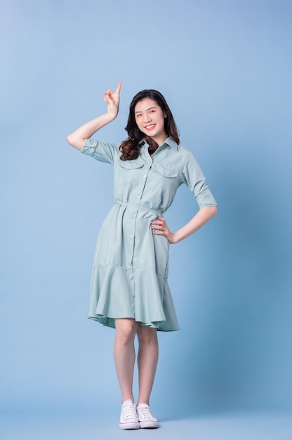 Full length image of young Asian woman wearing dress on blue background