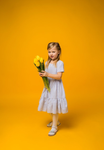 A full-length little girl stands with a bouquet of yellow tulips on yellow