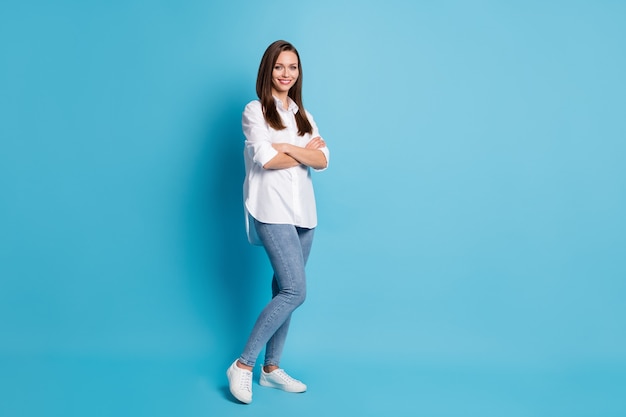 Full length photo of attractive lady arms crossed good mood wear white shirt jeans shoes isolated blue color background