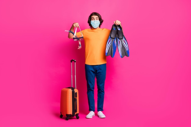 Full length photo of guy luggage show mask flips wear medical mask t-shirt jeans isolated pink color background