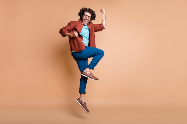 Full length photo portrait of ecstatic screaming man jumping up isolated on pastel beige colored background