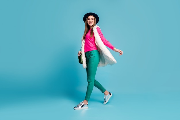 Full length photo of pretty modern stylish look lady walking down street tourist traveler good mood wear vintage hat trousers fur vest pink jumper isolated blue wall