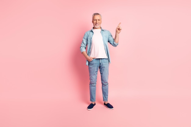 Full length photo of senior man indicate finger empty space advertise promotion isolated over pink color background.