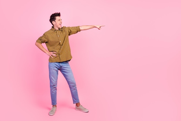 Full length photo of smiling young man pointing fingers empty space aside in isolated studio light pastel background