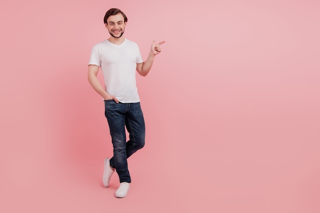 Full length photo of young glad guy showing finger copy empty blank place space ad advert isolated on pink color background