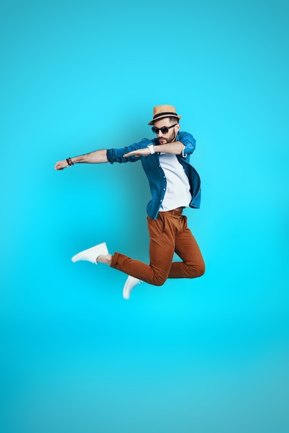 Full length of playful young man dancing while hovering against blue wall