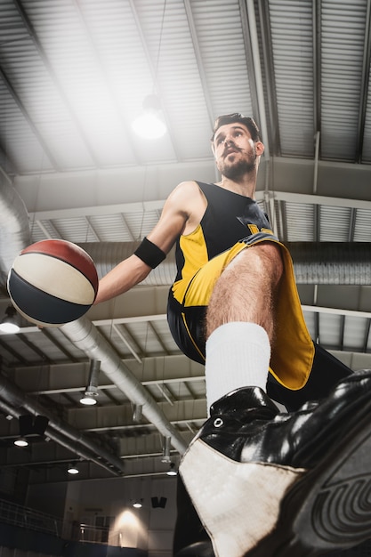 Full length portrait of a basketball player with a ball against gray gym background