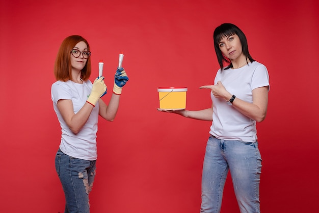 Full length portrait of beautiful ladies in a white t-shirts using gloves and paints. Isolated on red background