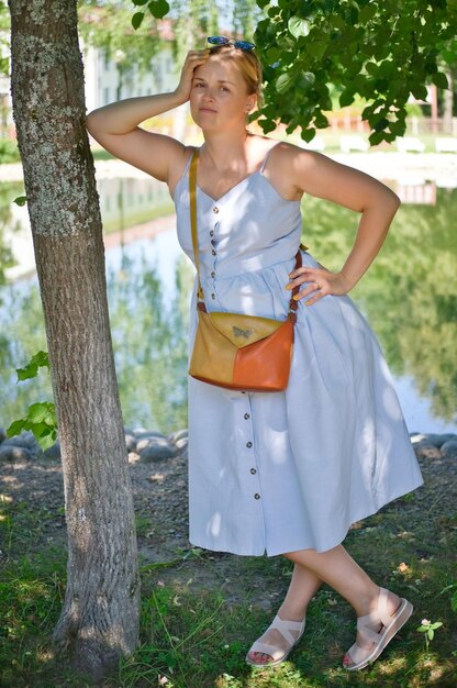 Full length portrait of beautiful woman in long blue dress near tree at summer sunny day