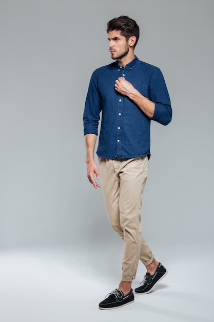 Full length portrait of a casual young man fastening button isolated on a gray wall