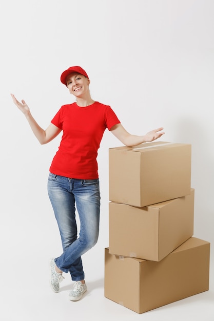 Full length portrait of delivery woman in red cap, t-shirt isolated on white background. Female courier or dealer standing near empty cardboard boxes. Receiving package. Copy space for advertisement.