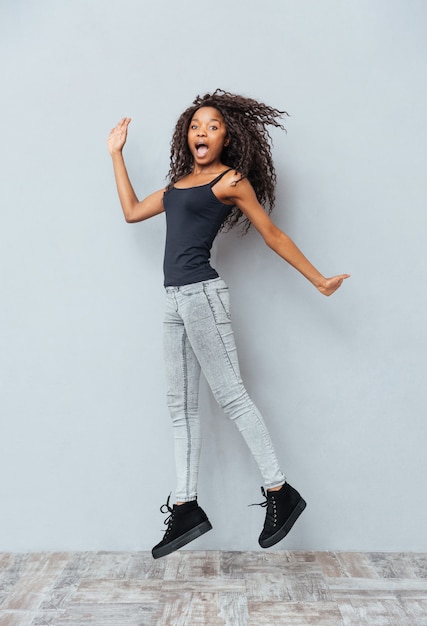 Full length portrait of a funny woman jumping on gray wall