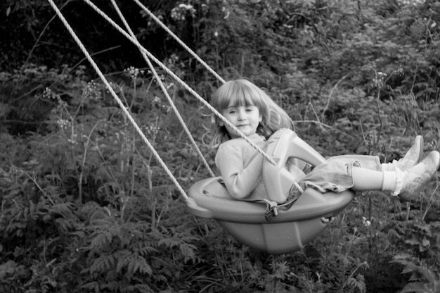 Photo full length portrait of girl sitting in swing against plants