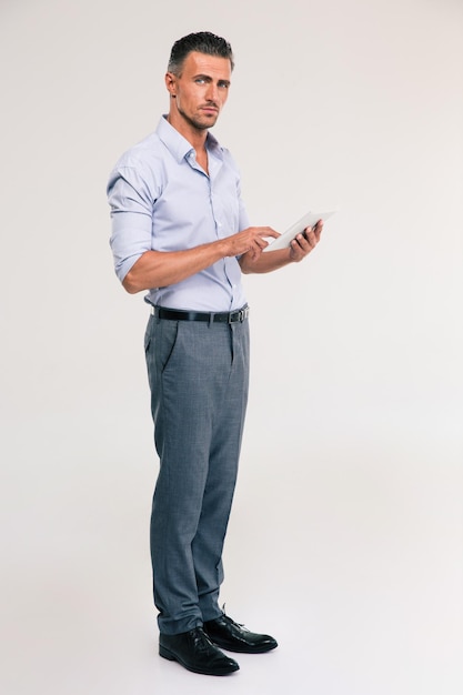 Photo full length portrait of a handsome man using tablet computer isolated. looking at camera