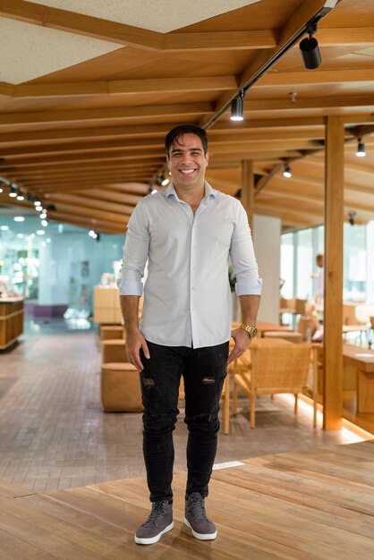 Full length portrait of handsome Persian man smiling and standing in coffee shop