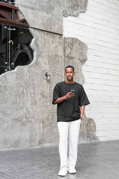 Full length portrait of handsome young African man using phone outdoors