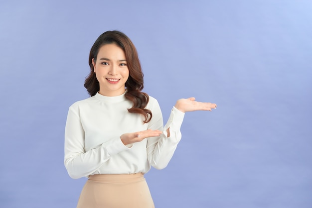 Full length portrait of a happy thoughtful woman holding copyspace on the palm isolated on a purple background