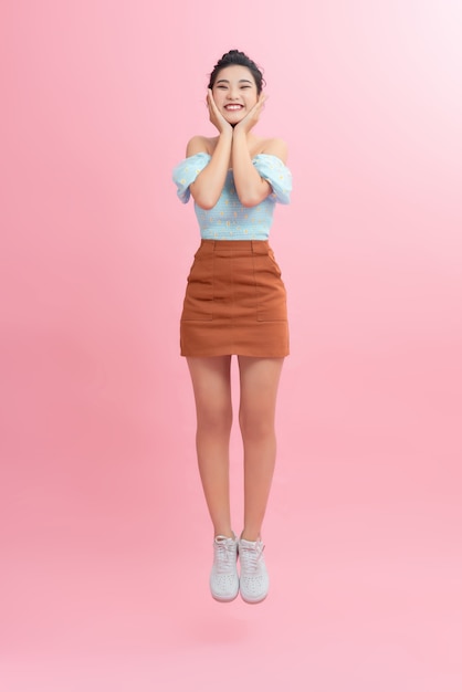 Full length portrait of a joyful young woman jumping and celebrating over pink background