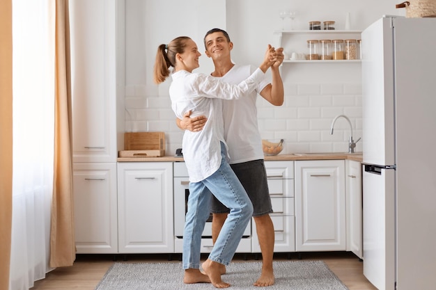 Full length portrait of man and attractive young adult woman dancing kitchen romantic couple spending time together at home expressing love and gentle