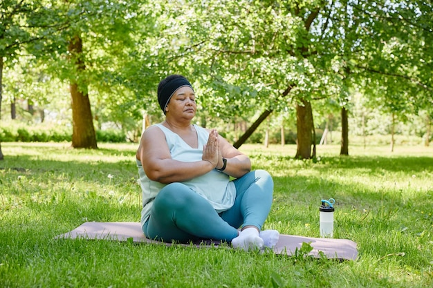 Full length portrait of overweight black woman doing yoga outdoors and meditating with eyes closed i