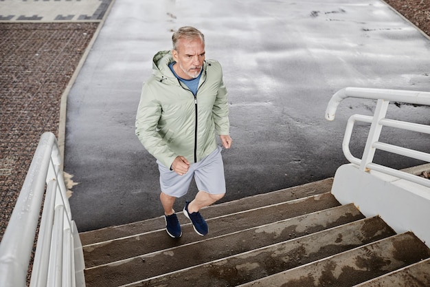 Full length portrait of senior man running up stairs outdoors in urban city setttting copy space