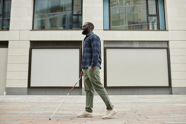 Full length portrait of smiling blind man walking in city and using cane copy space