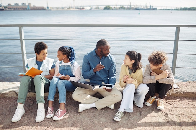 Full length portrait of smiling male teacher with diverse group of children enjoying outdoor class b