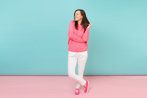 Full length portrait of smiling young woman in knitted rose sweater, white pants posing 