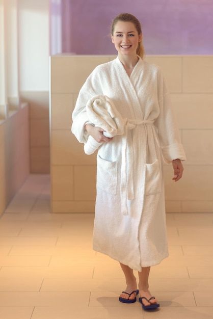 Full length portrait of smiling young woman wearing bathrobe standing at spa