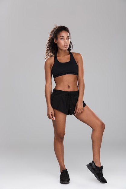 Full length portrait of a strong afro american sportswoman isolated over gray wall, standing