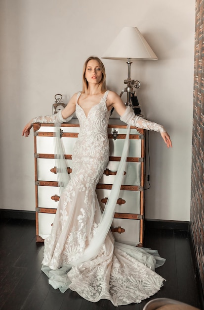 Full length portrait of young bride in elegant long dress posing in luxurious apartments