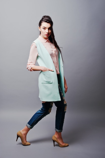 Full-length portrait young brunette girl wearing in pink blouse, turquoise jacket, ripped jeans and cream shoes