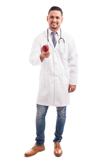 Full length portrait of a young Latin nutriologist in a lab coat holding an apple against a white background