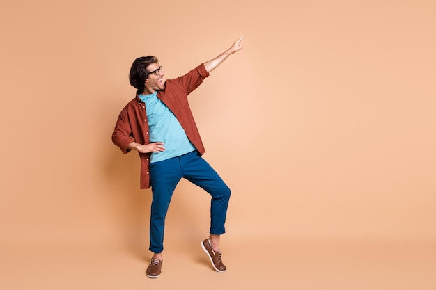 Full length profile photo of guy dance direct finger up wear spectacles brown t-shirt pants footwear isolated beige color background