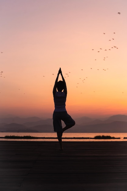 Full length rear view of woman standing on one leg while doing yoga at sunrise