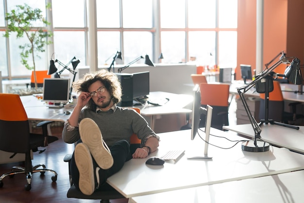 Full length of a relaxed casual young businessman sitting with legs on desk at office