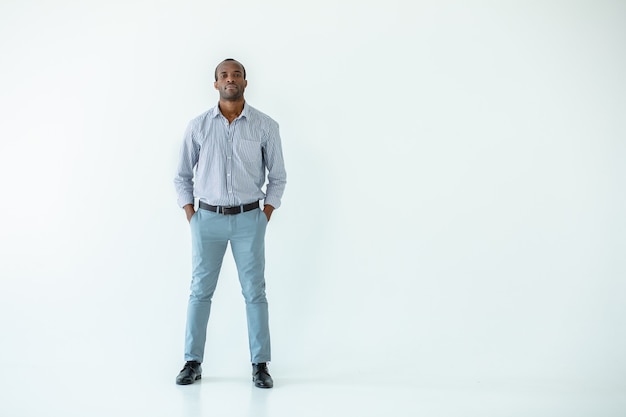 Full length of serious Afro american man holding his hands in the pocket while standing against white wall