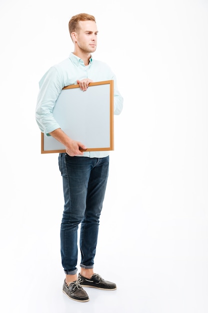 Photo full length of serious redhead young man standing and holding whiteboard